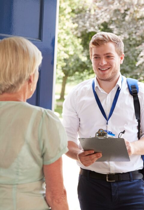 Senior woman opens door to male charity worker doing survey